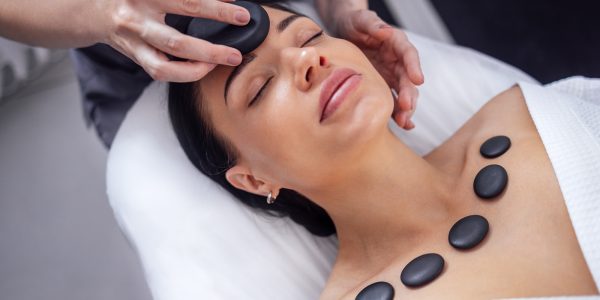 Close-up of a portrait of a young woman with her eyes closed rec Close-up of a portrait of a young woman with her eyes closed receiving a facial massage with hot stones. A beautiful girl lies and relaxes during a spa procedure. Taking care of yourself concert.